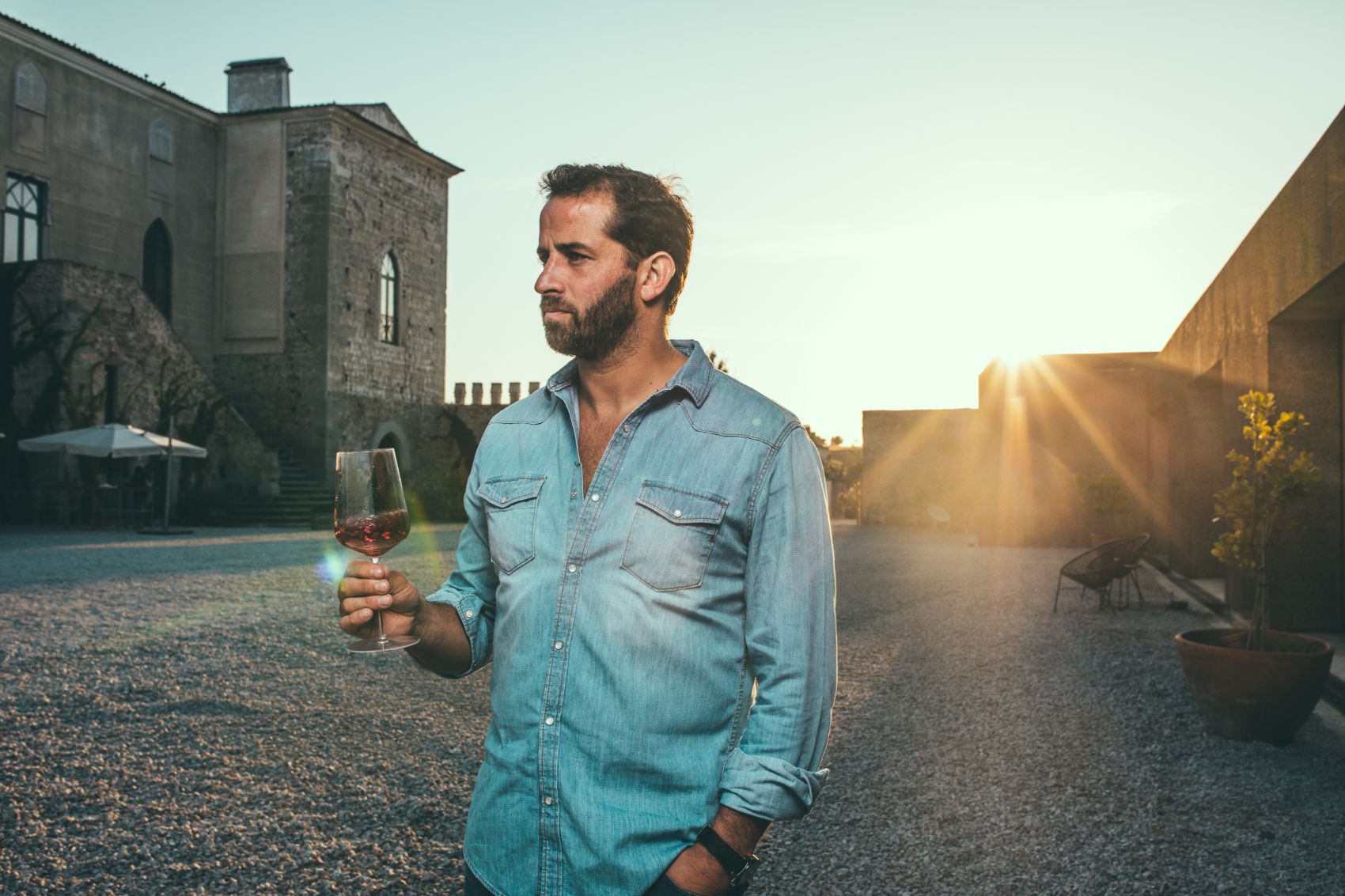 António Maçanita holds a glass of red wine, on the patio of Fitapreta, with the sunset behind.